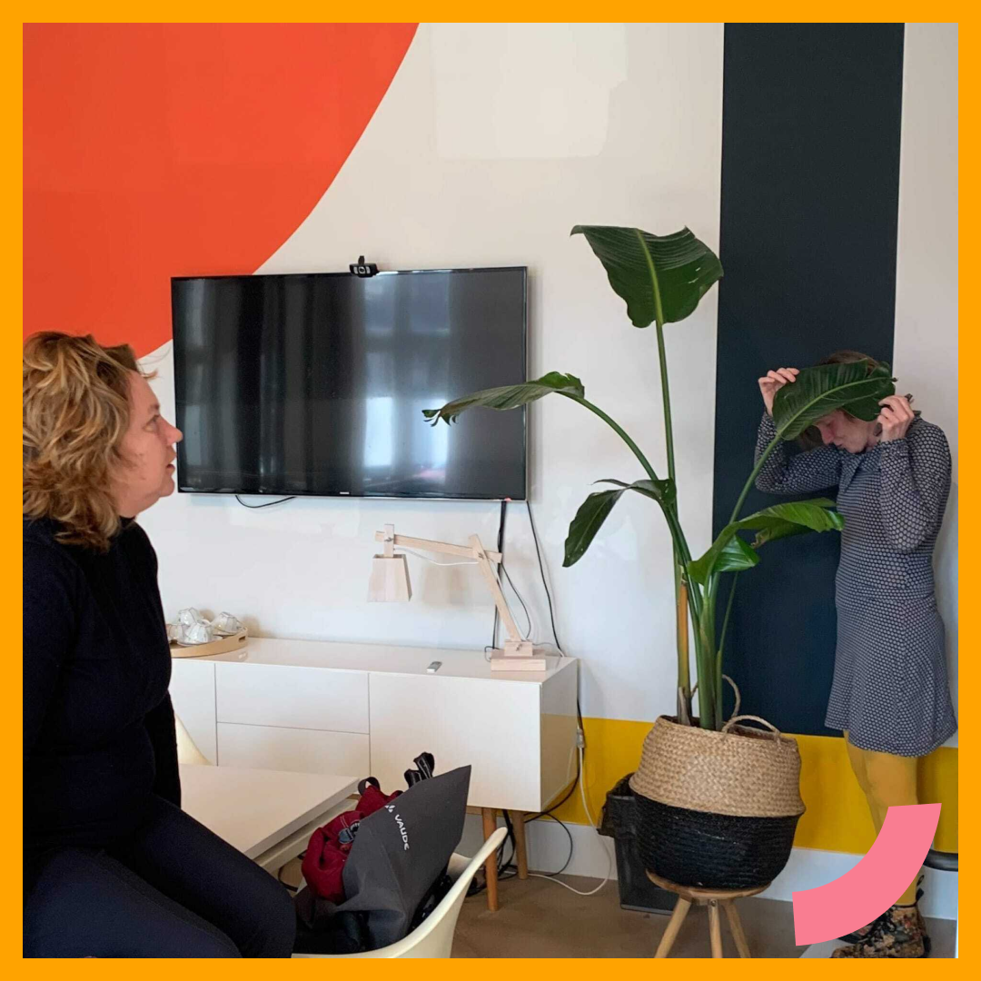 Jacqueline en Bettine doen een oefening. Jacqueline staat onder het blad van een grote plant.